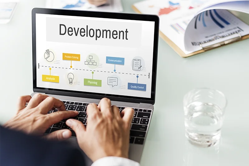 Graphic illustrating custom software development solutions featuring a laptop with data analytics and figures in a futuristic setting. 